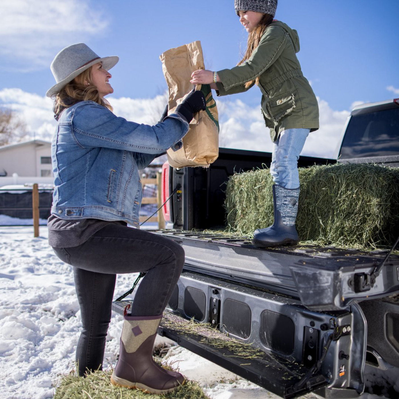 Woman and child loading hay into a truck bed on a snowy day