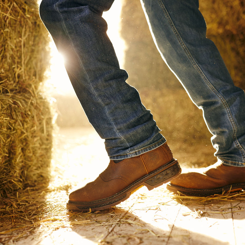 Close-up of legs wearing blue jeans and brown boots standing on hay with a blurred background