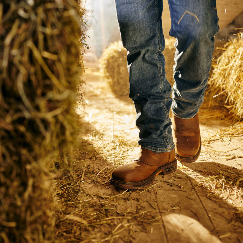 Person wearing blue jeans and brown boots standing on a hay bale.