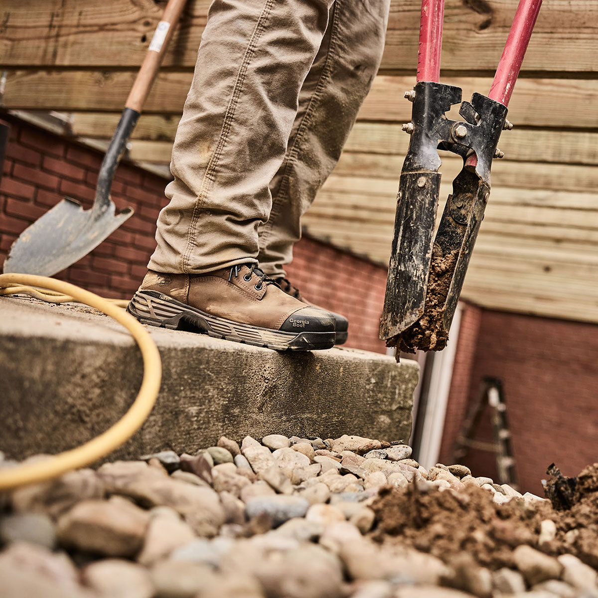 Person wearing work boots on a construction site with tools and gravel.