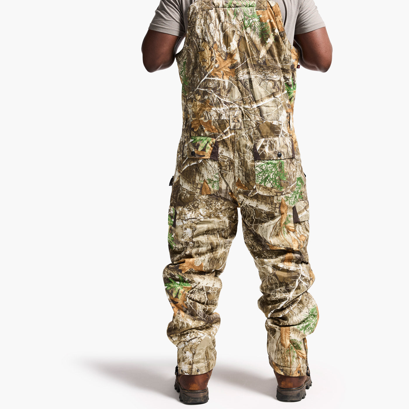 Camouflage bib overalls worn by a person on a white background
