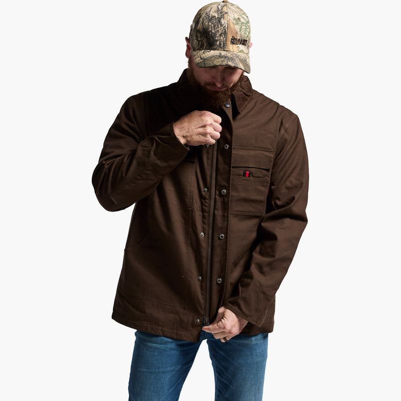 Man wearing a brown jacket, blue jeans, and a camouflage cap on a white background