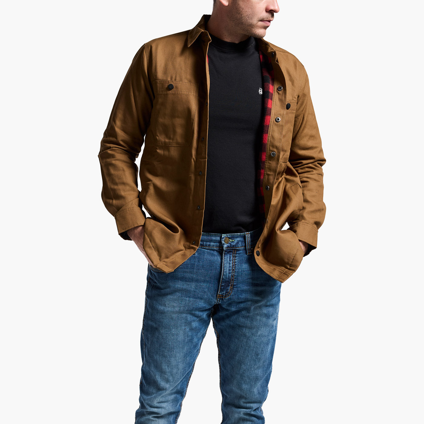 Man wearing a brown jacket over a black shirt with a plaid pattern, blue jeans, on a white background.